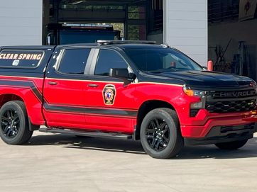A red Chevrolet truck with black accents, marked with the Clear Spring Fire Rescue emblem on the side, is parked outside a garage. The truck has black wheels and a canopy over the bed.